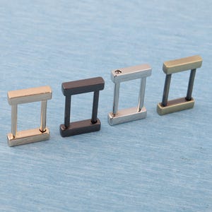 May include: Four metal rectangle connectors in gold, black, silver, and bronze. Each connector has a rectangular top and bottom piece connected by two vertical bars, creating a rectangular loop. The connectors are arranged diagonally on a blue surface.