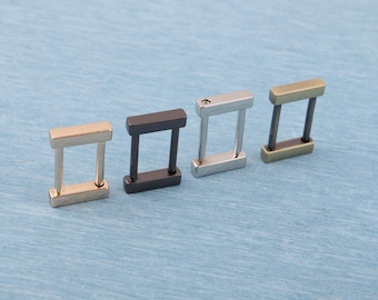 Può includere: Quattro connettori rettangolari in metallo color oro, nero, argento e bronzo. Ogni connettore ha una parte superiore e inferiore rettangolare collegata da due barre verticali, creando un anello rettangolare.