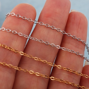 May include: Close-up of three delicate chain necklaces in gold and silver. The chains are made of small, oval links. The gold chain is at the bottom, the silver chain is at the top, and a silver chain is in the middle.