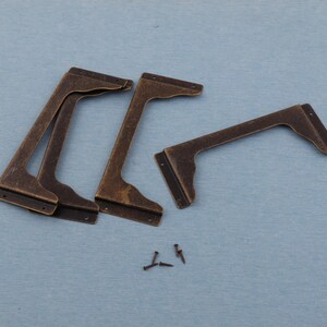 May include: A set of four antique bronze-colored shelf brackets with a decorative curved design. The brackets are L-shaped, with pre-drilled holes for mounting. Several small screws are also included.