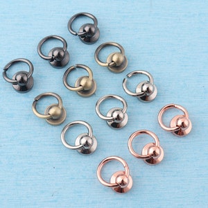 K&ouml;nnte beinhalten: Sortiment aus Metallringen mit einer Kugel oben. Die Ringe sind in verschiedenen Ausf&uuml;hrungen, darunter Silber, Gold und Schwarz.