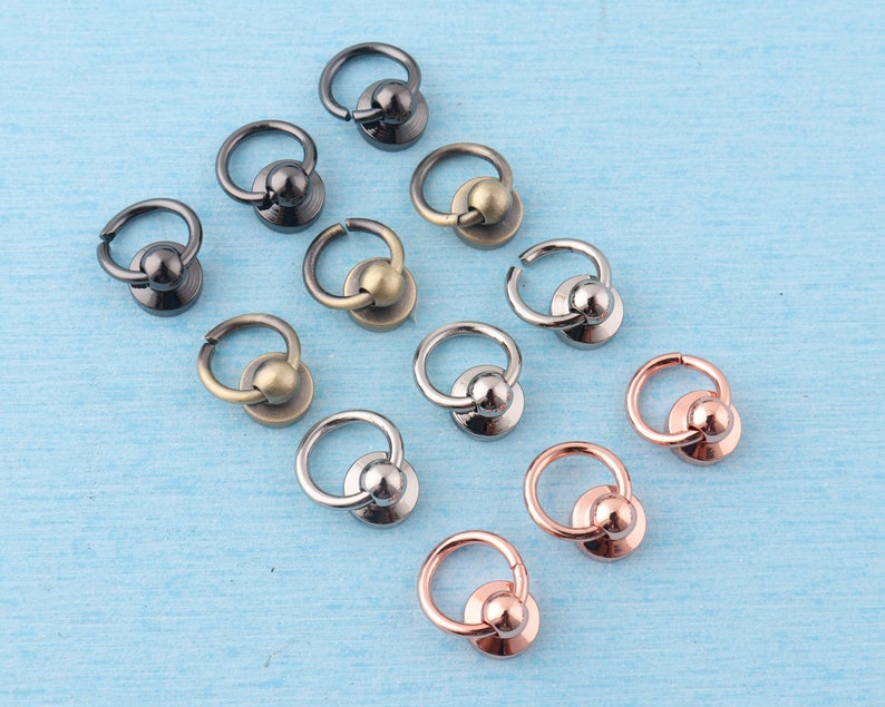 K&ouml;nnte beinhalten: Sortiment aus Metallringen mit einer Kugel oben. Die Ringe sind in verschiedenen Ausf&uuml;hrungen, darunter Silber, Gold und Schwarz.