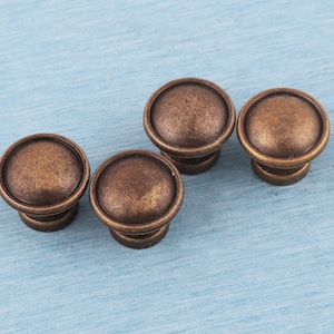 May include: Four antique bronze cabinet knobs with a rounded top and a textured surface. The knobs are set against a light blue background, creating a vintage aesthetic. These knobs are ideal for adding a touch of classic style to furniture.