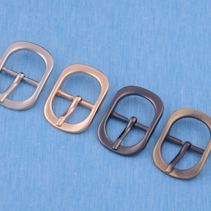 May include: Five metal belt buckles in different finishes: silver, gold, black, and antique brass. Each buckle has a classic oval shape with a smooth, polished surface.