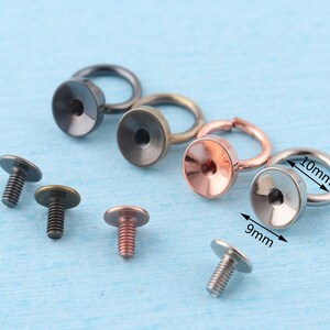 K&ouml;nnte beinhalten: Sortiment aus Metallringen und Schrauben in Silber-, Schwarz- und Kupferfarben. Die Ringe haben einen Durchmesser von 9 mm und 10 mm. Die Schrauben haben flache K&ouml;pfe und sind etwa 1 Zoll lang.