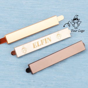 May include: Three metal bar clasps in gold, rose gold, and bronze. The center clasp is off-white with the word "ELFIN" in gold lettering and a small fairy graphic. The other two clasps are solid colors.