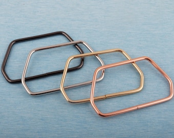 May include: Four metal purse frame handles in black, silver, gold, and copper colors. Each handle has a unique finish and a rectangular shape with rounded corners. The handles are arranged on a light blue textured surface.