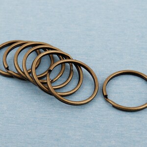 Puede incluir: Un juego de ocho llaveros de metal de color dorado. Los llaveros son todos del mismo tamaño y están dispuestos en círculo.