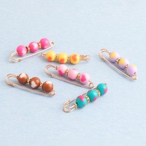 Może przedstawiać: Zestaw trzech ceramicznych kubków z nakrapianym, matowym wykończeniem. Kubki są w odcieniach kremu, jasnoszarym i ciemnoszarym. Każdy kubek ma prosty, minimalistyczny design.