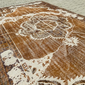 Puede incluir: Una alfombra vintage con un aspecto descolorido y desgastado. La alfombra tiene un fondo marr&oacute;n con un patr&oacute;n floral blanco. La alfombra est&aacute; hecha de lana y tiene una textura tejida a mano.