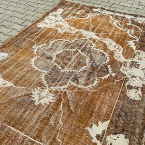 Puede incluir: Una alfombra vintage con un patr&oacute;n floral marr&oacute;n y blanco. La alfombra tiene un aspecto desgastado y est&aacute; hecha de un material suave y tejido.
