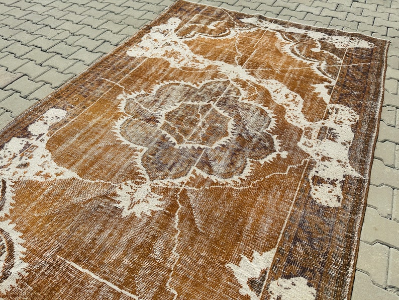 Puede incluir: Una alfombra vintage con un patr&oacute;n floral marr&oacute;n y blanco. La alfombra tiene un aspecto desgastado y est&aacute; hecha de un material suave y tejido.