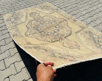 May include: A vintage cream-coloured rug with a dark grey and pink floral pattern. The rug has a fringed edge and is folded in half.
