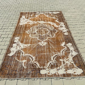 Puede incluir: Una alfombra vintage marr&oacute;n y blanca con un patr&oacute;n floral. La alfombra tiene un aspecto desgastado y est&aacute; hecha de lana.