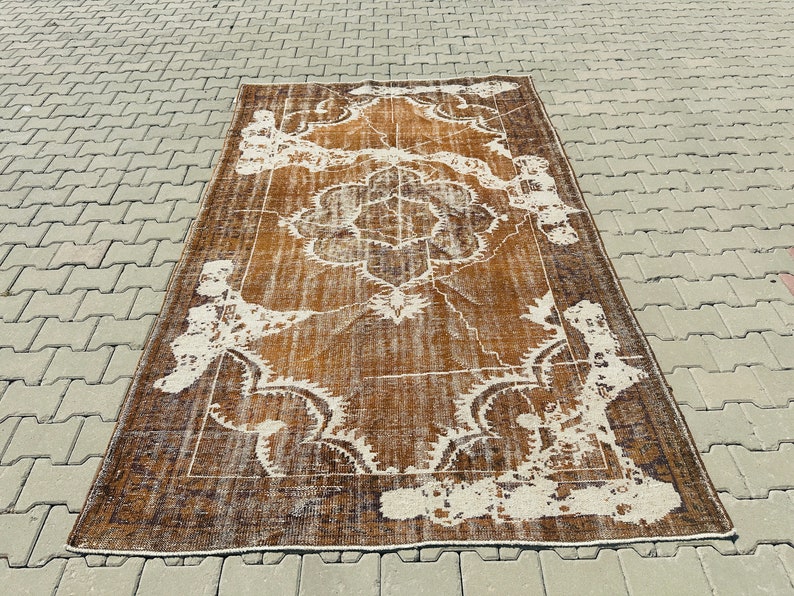 Puede incluir: Una alfombra vintage marr&oacute;n y blanca con un patr&oacute;n floral. La alfombra tiene un aspecto desgastado y est&aacute; hecha de lana.