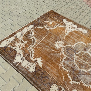 Puede incluir: Una alfombra vintage con un patr&oacute;n floral marr&oacute;n y blanco. La alfombra tiene un aspecto desgastado y est&aacute; hecha de lana.