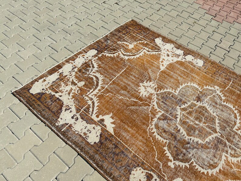 Puede incluir: Una alfombra vintage con un patr&oacute;n floral marr&oacute;n y blanco. La alfombra tiene un aspecto desgastado y est&aacute; hecha de lana.