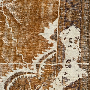 Puede incluir: Primer plano de una alfombra de color marr&oacute;n y blanco con un dise&ntilde;o descolorido. La alfombra tiene un aspecto desgastado y envejecido, lo que le da un toque vintage.