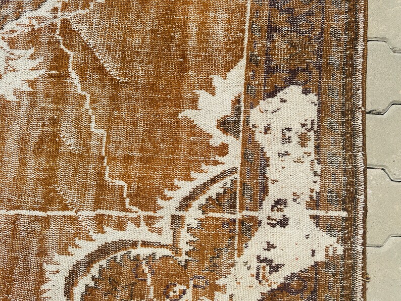 Puede incluir: Primer plano de una alfombra de color marr&oacute;n y blanco con un dise&ntilde;o descolorido. La alfombra tiene un aspecto desgastado y envejecido, lo que le da un toque vintage.