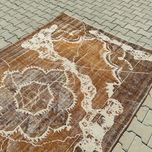 Puede incluir: Una alfombra vintage con un patr&oacute;n floral marr&oacute;n y blanco. La alfombra tiene un aspecto desgastado y est&aacute; hecha de un material suave y tejido.