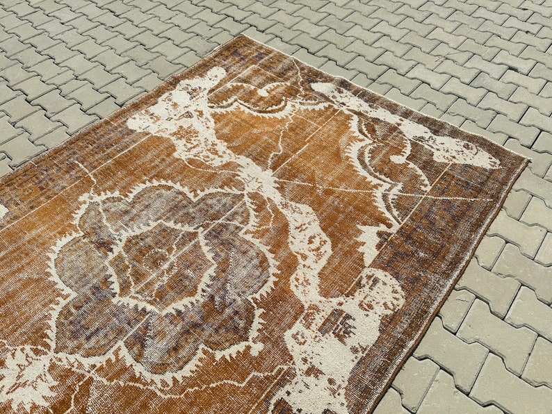 Puede incluir: Una alfombra vintage con un patr&oacute;n floral marr&oacute;n y blanco. La alfombra tiene un aspecto desgastado y est&aacute; hecha de un material suave y tejido.