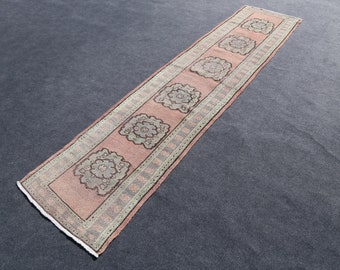 Puede incluir: Una alfombra larga y estrecha con fondo rosa y un patrón repetido de diseños florales verdes. La alfombra tiene un borde blanco con un pequeño patrón repetido.