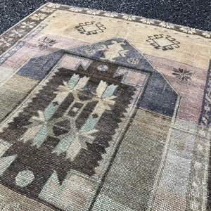 Puede incluir: Una alfombra vintage con un patrón geométrico en tonos marrones, beige y rosa. La alfombra tiene un aspecto descolorido y desgastado, lo que le da un encanto único y rústico.