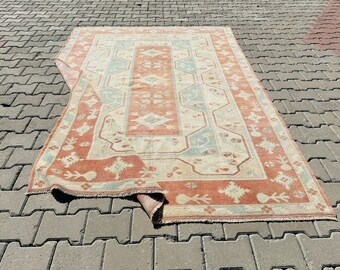 Puede incluir: Una alfombra vintage con un diseño persa tradicional en tonos melocotón, crema y azul. La alfombra está doblada por la mitad y se encuentra sobre una superficie de hormigón gris.