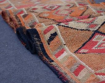 Puede incluir: Primer plano de una alfombra plegada con estampado naranja, rojo y negro con flecos azul oscuro.
