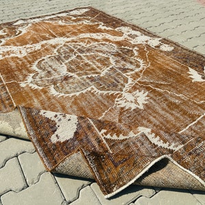 Puede incluir: Una alfombra vintage con un patr&oacute;n marr&oacute;n y blanco. La alfombra tiene un aspecto desgastado y est&aacute; doblada por la mitad.