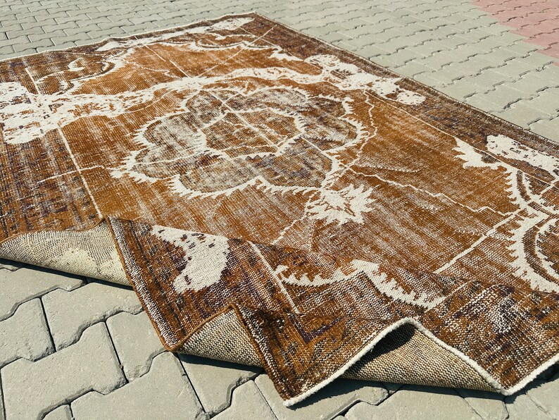 Puede incluir: Una alfombra vintage con un patr&oacute;n marr&oacute;n y blanco. La alfombra tiene un aspecto desgastado y est&aacute; doblada por la mitad.