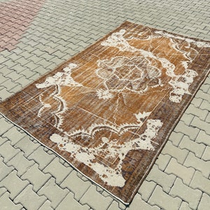 Puede incluir: Una alfombra vintage con un patr&oacute;n floral marr&oacute;n y blanco. La alfombra tiene un aspecto desgastado y est&aacute; hecha de lana.