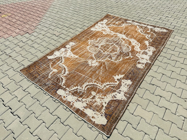 Puede incluir: Una alfombra vintage con un patr&oacute;n floral marr&oacute;n y blanco. La alfombra tiene un aspecto desgastado y est&aacute; hecha de lana.