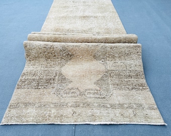 May include: A beige and brown vintage rug with a faded geometric pattern. The rug is rolled up and has a fringed edge.