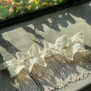 May include: A white lace trim with a silver fringe. The lace is delicate and has a ruffled edge. The fringe is made of thin silver chains.