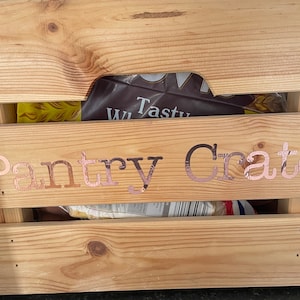 Könnte beinhalten: Eine Holzkiste mit der Aufschrift "Pantry Crate" in roségoldenen Lettern. Die Kiste ist mit verschiedenen Lebensmitteln gefüllt.