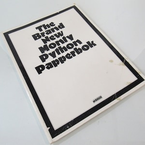 May include: A vintage book titled "The Brand New Monty Python Papperbok" with a white cover and black text. The book has a black border and the Mandarin logo. The book is slightly worn.