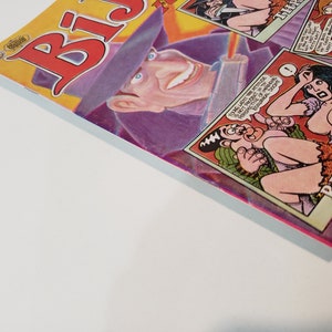 Puede incluir: Un c&oacute;mic con una portada vibrante, con un gran t&iacute;tulo rojo e ilustraciones de dibujos animados. La portada incluye un hombre sonriente con un sombrero morado y vi&ntilde;etas de c&oacute;mic con figuras escasamente vestidas.