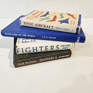 May include: A stack of four vintage books about airplanes. The top book is titled "Basic Aircraft - Military" and is cream colored with blue lettering. The second book is blue with white lettering and is titled "Warplanes of the World". The third book is white with blue lettering and is titled "Fighters Volume Four". The bottom book is black with white lettering and is titled "War Planes Fighters 4 Doubleday".