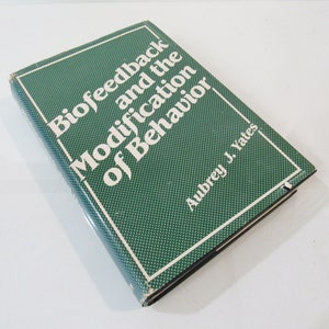 May include: A hardcover book titled "Biofeedback and the Modification of Behavior" by Aubrey J. Yates. The book has a green cover with a white dotted pattern and white text. The book is slightly angled.