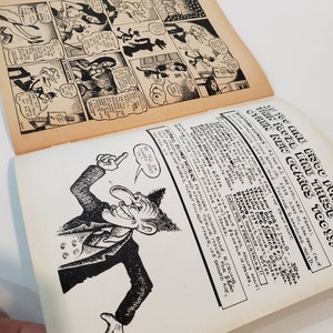 May include: Open vintage comic book pages with black and white illustrations. One page features a comic strip with speech bubbles, while the other displays a cartoon character and text. The pages are aged with a yellowed tone.