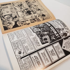 Puede incluir: P&aacute;ginas de c&oacute;mic abiertas con ilustraciones y texto en blanco y negro. La p&aacute;gina superior presenta una tira c&oacute;mica. La p&aacute;gina inferior contiene anuncios y el texto "BACK ISSUES!"