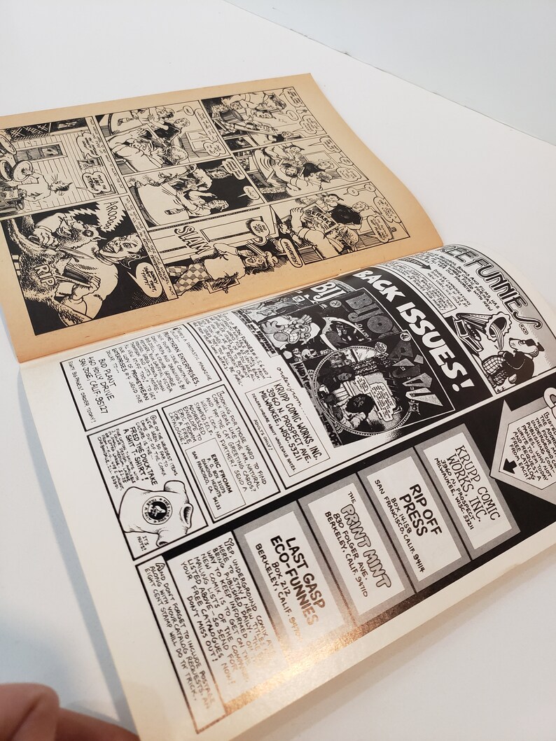 Puede incluir: P&aacute;ginas de c&oacute;mic abiertas con ilustraciones y texto en blanco y negro. La p&aacute;gina superior presenta una tira c&oacute;mica. La p&aacute;gina inferior contiene anuncios y el texto "BACK ISSUES!"
