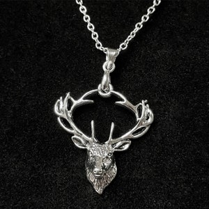May include: Silver necklace featuring a detailed deer head pendant. The deer has antlers that form a circle around the head.