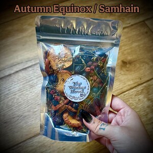 May include: A transparent bag containing dried fruits, berries, and herbs. The bag features a label with "The Witches Hovel." The text "Autumn Equinox / Samhain" is at the top. The contents are a mix of brown, red, and blue.