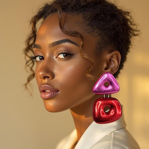 Puede incluir: Una mujer con el pelo oscuro y rizado lleva una camisa blanca y grandes pendientes geométricos de color rosa y rojo.