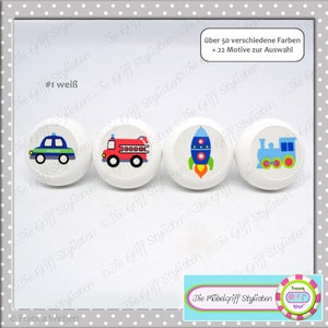 May include: Four white round knobs with colorful designs of a police car, fire truck, rocket ship, and train. The text "Die Möbelgriff Stylisten" is visible in the bottom right corner of the image.