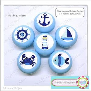 May include: Seven blue and white nautical themed knobs with various designs including an anchor, a ship's wheel, a lighthouse, a sailboat, a crab, and a fish. The knobs are labeled "Die Möbelgriff Stylisten" and "#23 blau mittel".