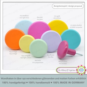 Könnte beinhalten: Sortiment an bunten Holzknöpfen in verschiedenen Farbtönen von Rosa, Blau, Grün, Gelb, Orange und Lila. Die Knöpfe sind rund und haben eine glatte, polierte Oberfläche. Der Text "Die Möbelgriff Stylisten" ist im Bild sichtbar.