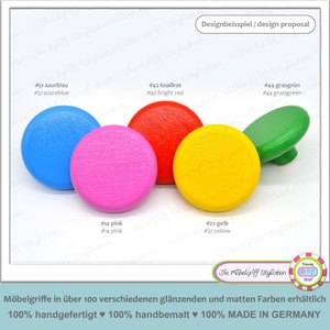 Puede incluir: Surtido de pomos de madera de colores en varios colores, incluyendo azul, rosa, amarillo, rojo y verde. Los pomos son redondos y tienen una superficie lisa y texturizada. El texto "Die Möbelgriff Stylisten" es visible en la esquina inferior derecha de la imagen.